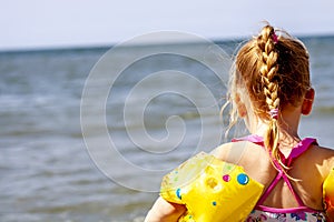 Happy little girl with floaties floaties preparing to swim in the ocean