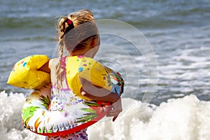 Happy little girl with floaties floaties preparing to swim in the ocean