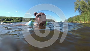 A happy little girl is floating on the river in inflatable armbands, on a bright sunny day, against a background of blue