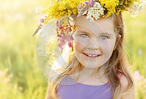 Happy little girl in flower crown on sunny summer meadow