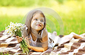 Happy little girl and flowers on the meadow in summer sunny day