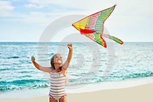 Happy little girl with flying kite on tropical beach