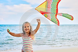Happy little girl with flying kite on tropical beach