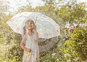 Happy little girl in garden under the summer rain with an umbrella