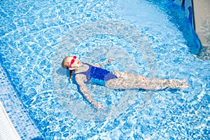 Happy little girl in goggles swim in swimming pool View from above