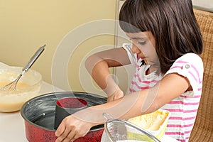 Happy little girl greasing a mold to bake a cake