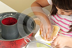 Happy little girl greasing a mold to bake a cake