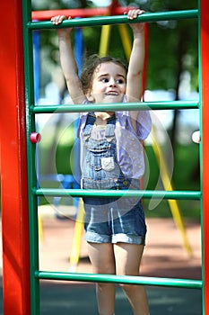Happy little girl hanging on gymnastic wall on the