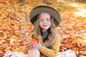 Happy little girl in hat and autumn clothes on an autumn background. A smiling child is playing in fall park.