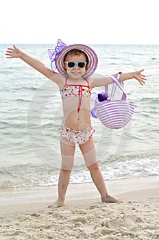 Happy little girl in a hat and sunglasses posing on the beach.