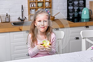 Happy little girl have breakfast in a white kitchen. She eats apple and smiling. Healthy eating