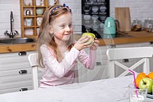 Happy little girl have breakfast in a white kitchen. She eats apple and smiling. Healthy eating