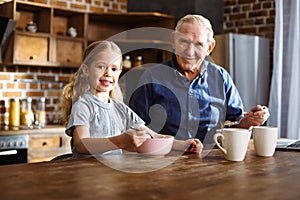 Happy little girl having breakfast with her grandfather