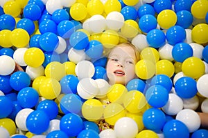 Happy little girl having fun in ball pit in kids indoor play center. Child playing with colorful balls in playground ball pool.