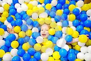 Happy little girl having fun in ball pit in kids indoor play center. Child playing with colorful balls in playground ball pool.