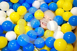 Happy little girl having fun in ball pit in kids indoor play center. Child playing with colorful balls in playground ball pool.