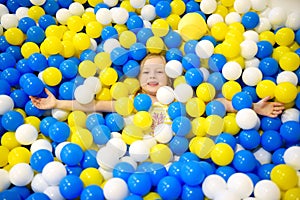 Happy little girl having fun in ball pit in kids indoor play center. Child playing with colorful balls in playground ball pool.