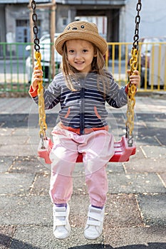 Happy little girl having fun on outdoor playground. Swinging on swing