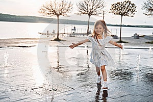 Happy little girl having fun outdoors in the fountain near the lake at summer