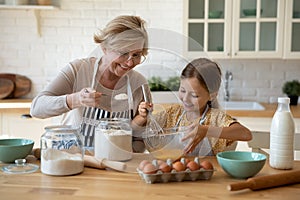 Happy little girl help senior grandma at kitchen mix dough