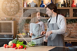 Happy Little Girl And Her Dad Making Fresh Veggie Salad In Kitchen