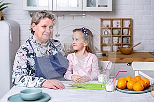 Happy little girl and her grandmother have breakfast together in a white kitchen. They are having fun and playing with fruits.