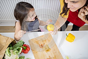 Little girl and her mother slicing vegetables on a cutting board