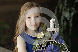 Happy little girl holding decorative bird cage full of flowers. Studio shot in provence style interior