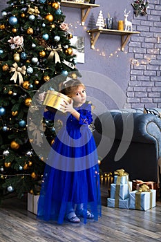 Happy little girl holding gift box by christmas tree Isolated.
