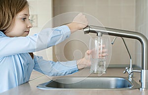 Happy little girl holding a glass of water. Selective focus on child hand with glass of water in foreground. Hydration. Healthy