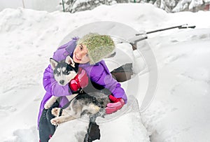 Happy little girl holding her puppy dog husky on the snow