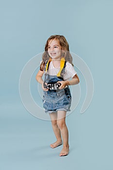 Happy little girl holding a vintage mirrored camera over blue background