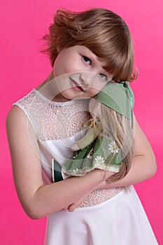 A happy little girl holds gently in arms her favorite doll in a green hat and a green dress