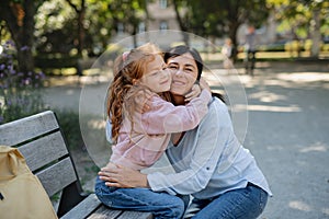 Happy little girl hugging her grandmother outdoors in park.
