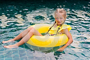 Happy little girl with inflatable rubber circle having fun in swimming pool