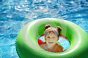 Happy little girl with inflatable toy ring float in swimming pool. Little preschool child learning to swim and dive in