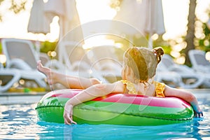 Happy little girl with inflatable toy ring float in swimming pool. Little preschool child learning to swim and dive in