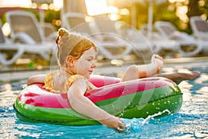 Happy little girl with inflatable toy ring float in swimming pool. Little preschool child learning to swim and dive in