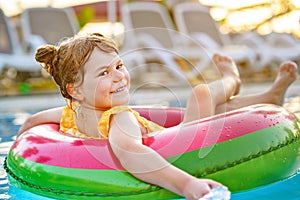 Happy little girl with inflatable toy ring float in swimming pool. Little preschool child learning to swim and dive in