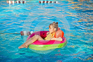 Happy little girl with inflatable toy ring float in swimming pool. Little preschool child learning to swim and dive in