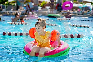 Happy little girl with inflatable toy ring float in swimming pool. Little preschool child learning to swim and dive in