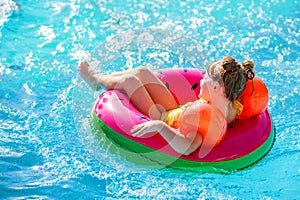 Happy little girl with inflatable toy ring float in swimming pool. Little preschool child learning to swim and dive in