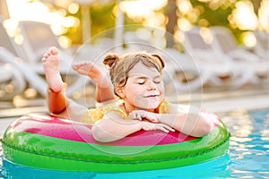 Happy little girl with inflatable toy ring float in swimming pool. Little preschool child learning to swim and dive in