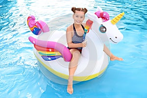 Happy little girl on inflatable unicorn in swimming