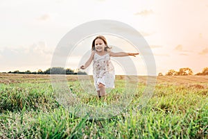 Happy little girl joyfully running across field. Carefree child on grassy meadow. Outdoor walking. Beautiful sunny sky.
