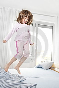Happy little girl jumping on a bed