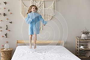 Happy little girl jumping on bed in modern bedroom