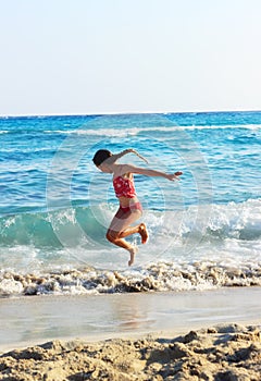 Happy Little Girl Jumping In Sea Waves. Jump Accompanied By Water Splashes. Summer Sunny Day, Ocean Coast