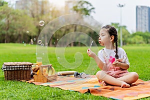 Happy little girl kid blowing soap bubbles playing alone in the park, Black hair style