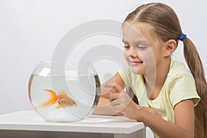 Happy little girl knocking his finger on the aquarium with goldfish